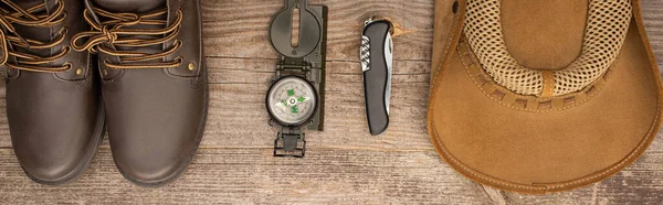 Panoramic shot of boots, compass, jackknife and hat on wooden table — Stock Photo