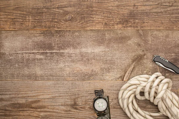 Vista superior de brújula, cuerda de senderismo y navaja sobre superficie de madera - foto de stock