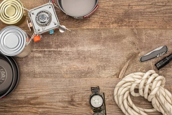 Vista superior de quemador de gas, platos de metal, latas de estaño y equipo de senderismo en mesa de madera - foto de stock