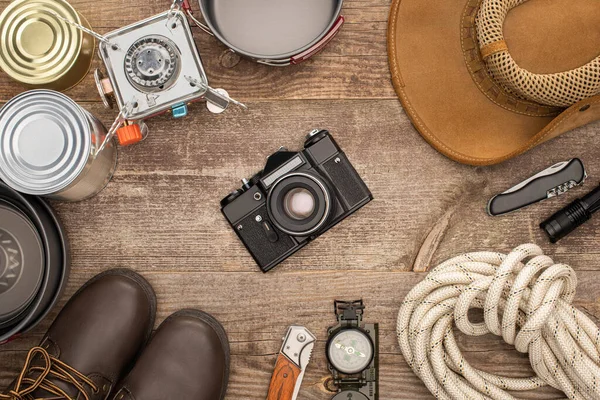 Vue de dessus de l'appareil photo, chapeau, bottes et matériel de randonnée sur table en bois — Photo de stock