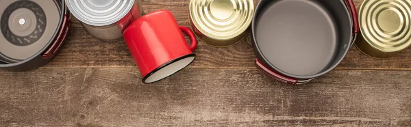 Plano panorámico de latas, platos de metal y taza sobre mesa de madera - foto de stock