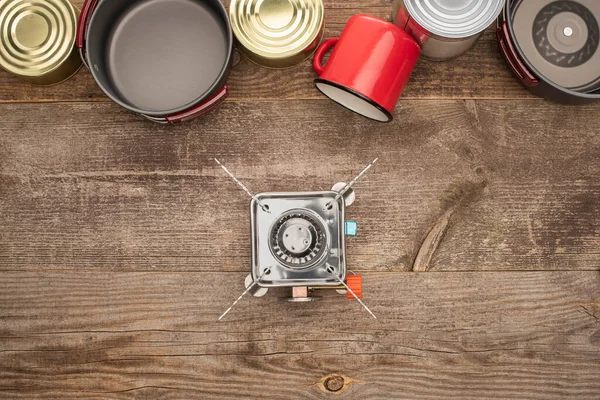 Vue de dessus des boîtes de conserve, brûleur à gaz, vaisselle en métal et tasse sur la surface en bois — Photo de stock