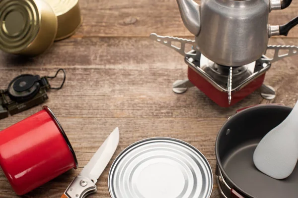 Vue rapprochée du brûleur à gaz, des boîtes de conserve, de la tasse en métal et du couteau à jackknife sur une table en bois — Photo de stock