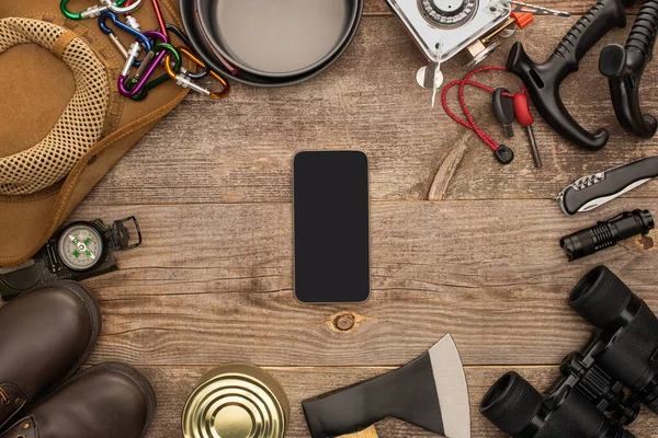 Vue du dessus du smartphone avec écran noir près de l'équipement de randonnée sur table en bois — Photo de stock