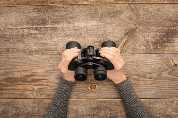 Partial view of woman holding binoculars on wooden table — Stock Photo