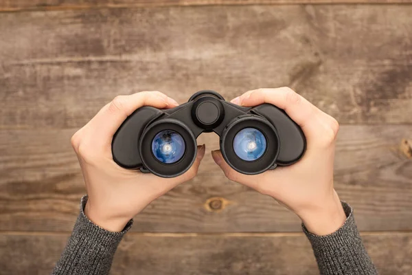 Selective focus of woman holding binoculars on wooden table — Stock Photo