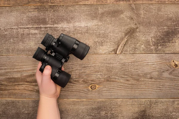 Partial view of man holding binoculars on wooden table — Stock Photo