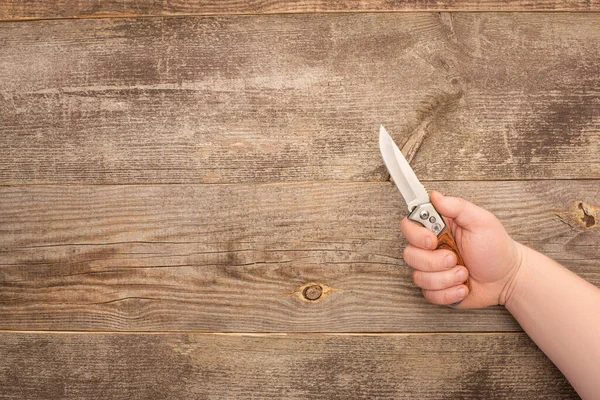 Partial view of man holding jackknife on wooden table — Stock Photo