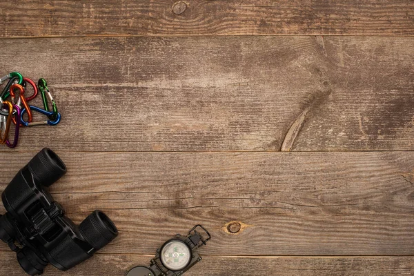 Top view of carabiners, binoculars and compass on wooden table — Stock Photo