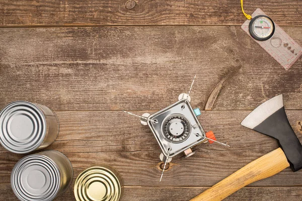 Top view of gas burner, axe, compass and canned goods on wooden surface — Stock Photo
