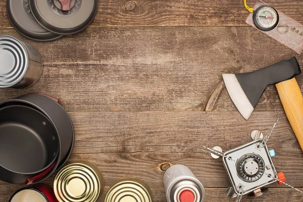 Вид зверху на олов'яні банки, металевий посуд, сокиру, газовий пальник і компас на дерев'яному столі — стокове фото