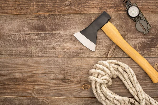 Vue de dessus de hache, corde de randonnée et boussole sur la surface en bois — Photo de stock