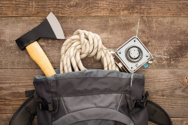 Vista superior de la mochila con hacha, cuerda de senderismo y quemador de gas en la mesa de madera - foto de stock