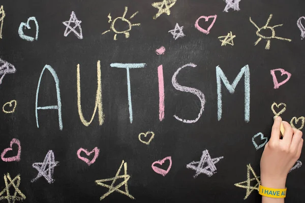 Partial view of woman drawing hearts, stars and suns on chalkboard with autism inscription — Stock Photo