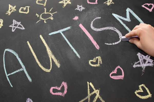 Partial view of woman writing word autism on chalkboard — Stock Photo