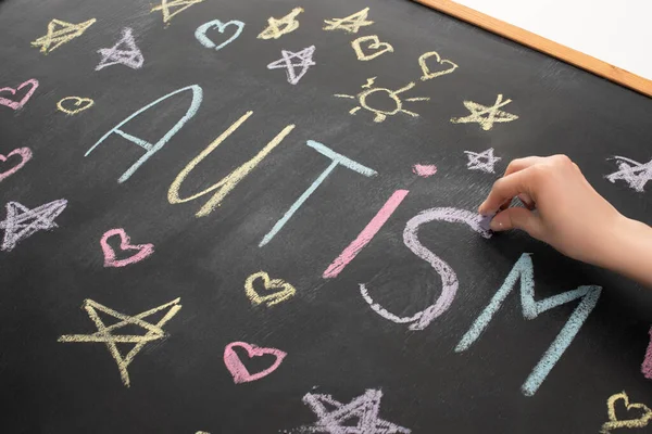 Visión parcial de la mujer escribiendo palabra autismo en pizarra con corazones, estrellas y soles - foto de stock