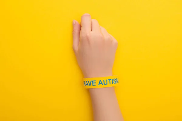 Top view of woman hand in bracelet with I have autism inscription on yellow — Stock Photo