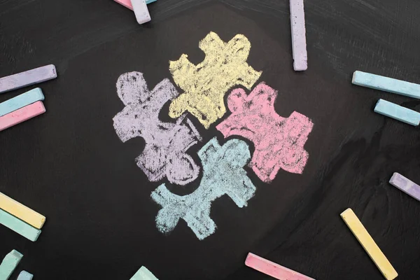 Top view of chalks on blackboard with puzzle drawing for World Autism Awareness Day — Stock Photo