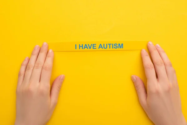 Partial view of woman holding bracelet with I have autism inscription on yellow — Stock Photo
