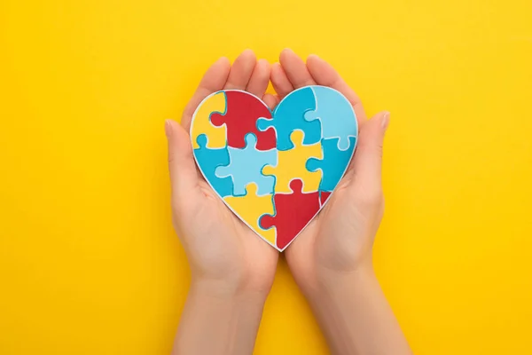 Partial view of woman holding puzzle heart on yellow — Stock Photo