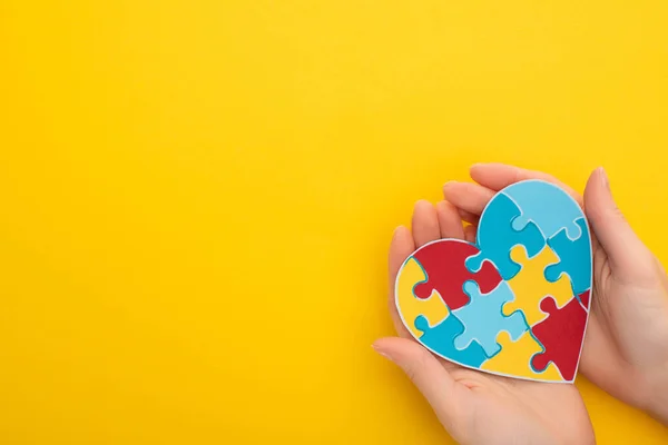 Vista parziale della donna che tiene colorato puzzle cuore sul giallo per la Giornata Mondiale della Consapevolezza Autismo — Foto stock