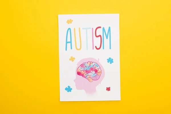 Вид зверху паперового листа з аутизмом написання і малюнок дитини ізольовані на жовтому — стокове фото