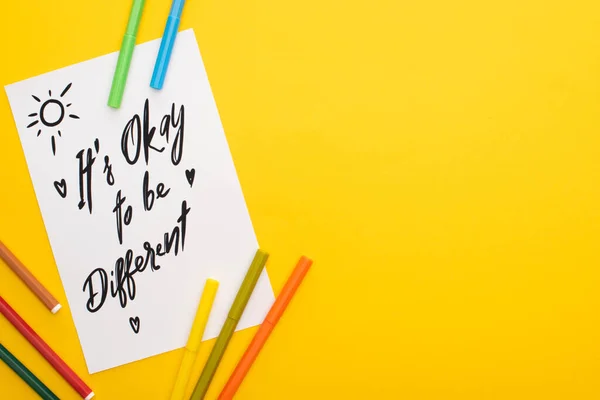 Top view of felt pens on paper sheet with its okay to be different inscription isolated on yellow — Stock Photo