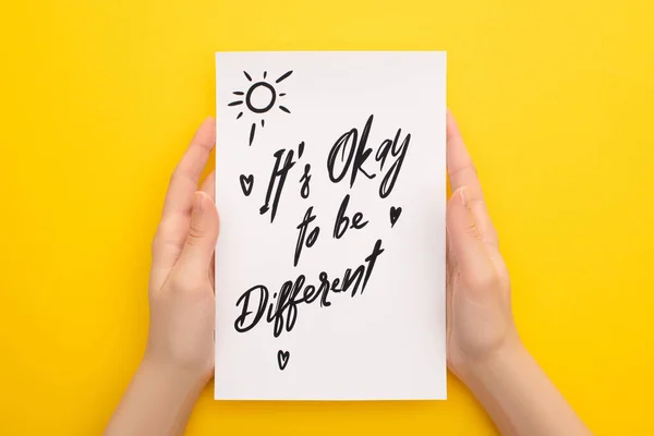 Cropped view of person holding sheet of paper with its okay to be different inscription on yellow — Stock Photo