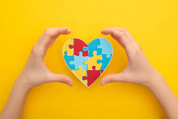 Обрезанный вид женских рук с сердцем-головоломкой на желтом на Всемирный день информирования об аутизме — стоковое фото