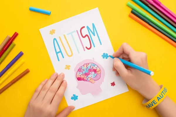 Vista recortada de la tarjeta de dibujo de la mujer con la cabeza, el cerebro y el rompecabezas para el Día de la conciencia del autismo en amarillo - foto de stock