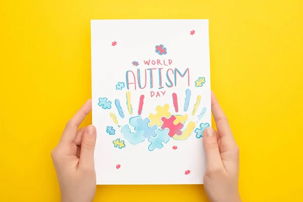 Visão recortada da mulher segurando cartão com quebra-cabeça e impressões de mão para o Dia Mundial do Autismo no amarelo — Fotografia de Stock