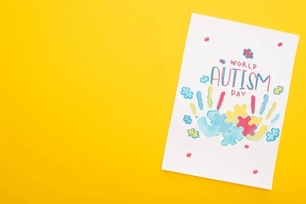 Top view of card with puzzle and hand prints for World Autism Day isolated on yellow — Stock Photo
