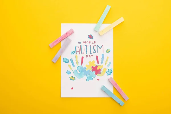 Top view of card with puzzle and hand prints for World Autism Day isolated on yellow with chalks — Stock Photo