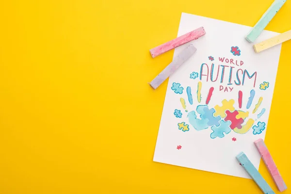 Top view of card with puzzle and hand prints for World Autism Day isolated on yellow with colorful chalks — Stock Photo