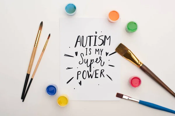 Vista superior de pinturas, pinceles y tarjetas con autismo es mi súper poder de letras en blanco - foto de stock