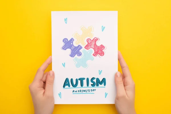 Vue recadrée de la femme tenant la carte avec puzzle pour la Journée de sensibilisation à l'autisme sur jaune — Photo de stock