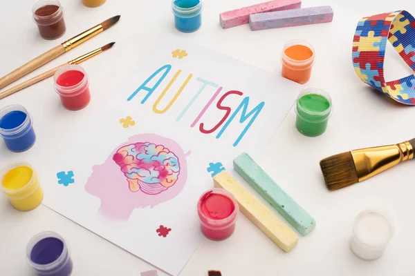 Tarjeta con autismo palabra y pintura de la cabeza con el cerebro en blanco con pinceles, tiza y pinturas - foto de stock