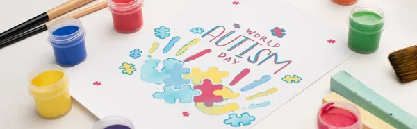 Панорамный снимок открытки с надписью ко Всемирному дню аутизма и покраской головоломок и отпечатков рук на белом с помощью кистей, мел и красок — стоковое фото