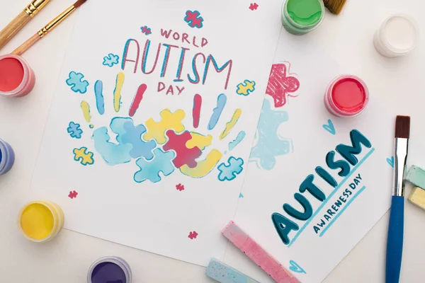 Top view of cards for World Autism Day lettering and painting of puzzle and hand prints on white with paint brushes, chalks and paints — Stock Photo