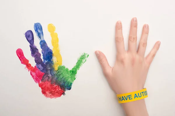 Vista recortada de la mano femenina con brazalete de autismo en blanco con colorida huella de mano - foto de stock