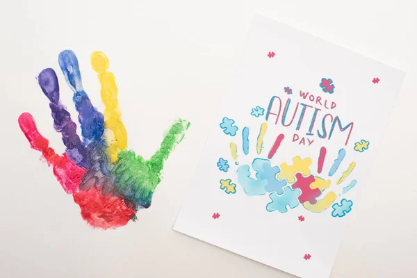 Top view of colorful handprint and card with puzzle and World Autism Day lettering on white — Stock Photo