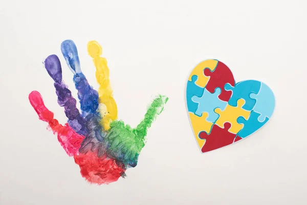 Vista superior de la huella de mano colorida y el corazón del rompecabezas en blanco para el Día Mundial de la Concienciación sobre el Autismo - foto de stock