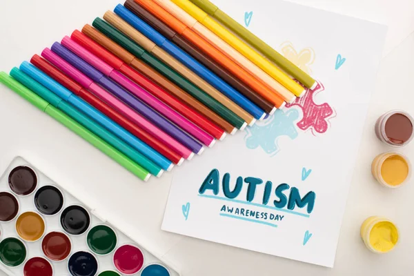Vista superior de la tarjeta con letras Autism Awareness Day y pintura de rompecabezas en blanco con marcadores y pinturas - foto de stock