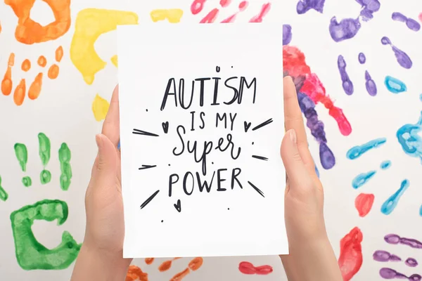 Cropped view of woman holding card with Autism is my super power lettering on white with hand prints — Stock Photo