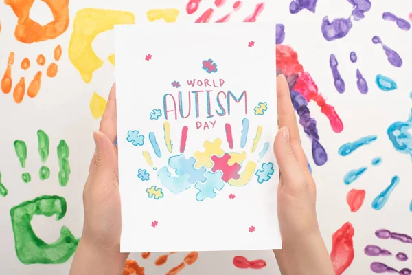 Vista recortada de la mujer que sostiene la tarjeta con letras Día Mundial del Autismo y rompecabezas en blanco con impresiones de mano — Stock Photo