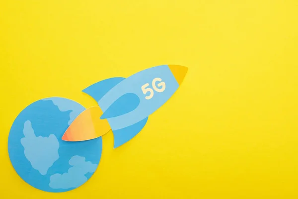 Top view of paper rocket with 5g lettering near globe on yellow background — Stock Photo