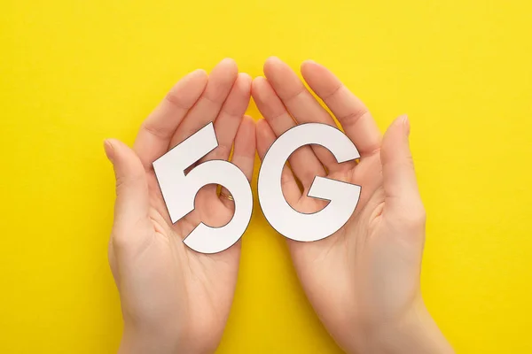 Cropped view of woman holding white 5g lettering on yellow background — Stock Photo