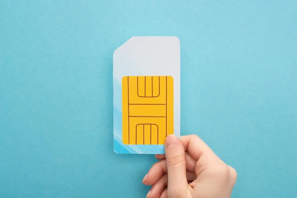 Cropped view of woman holding sim card on blue background — Stock Photo