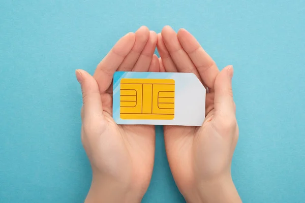 Vista cortada da mulher segurando cartão SIM no fundo azul — Fotografia de Stock