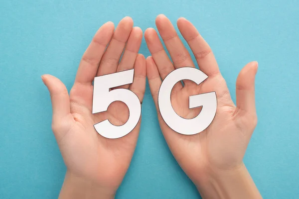 Cropped view of woman holding white 5g lettering on blue background — Stock Photo